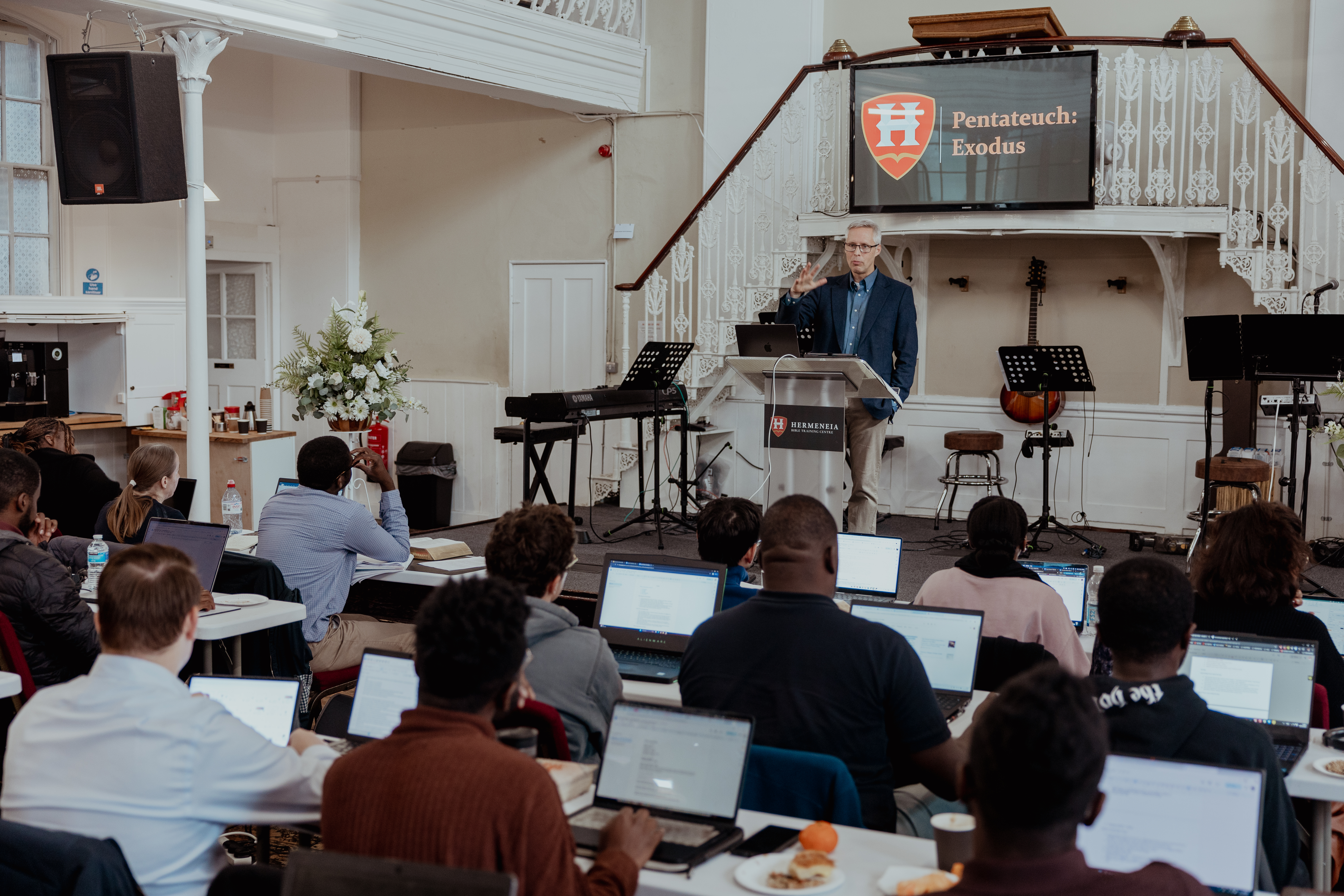 Students engaged in a Bible Survey course at Hermeneia Bible Training Centre, using tablets, Bibles, and notebooks in a focused classroom setting.